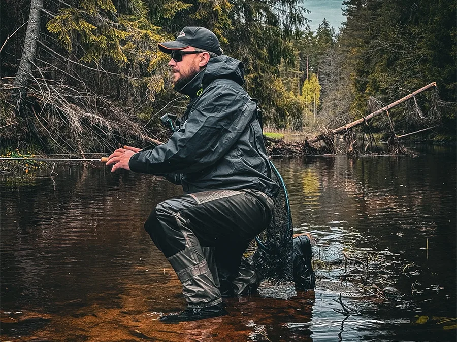 A person in waders fishing in a forest river among trees